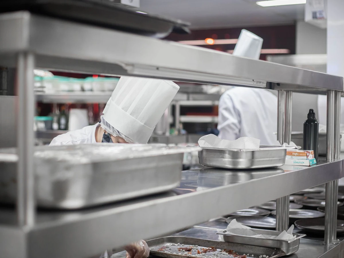 Cooks preparing food in a stainless steel commercial kitchen with overhead shelving