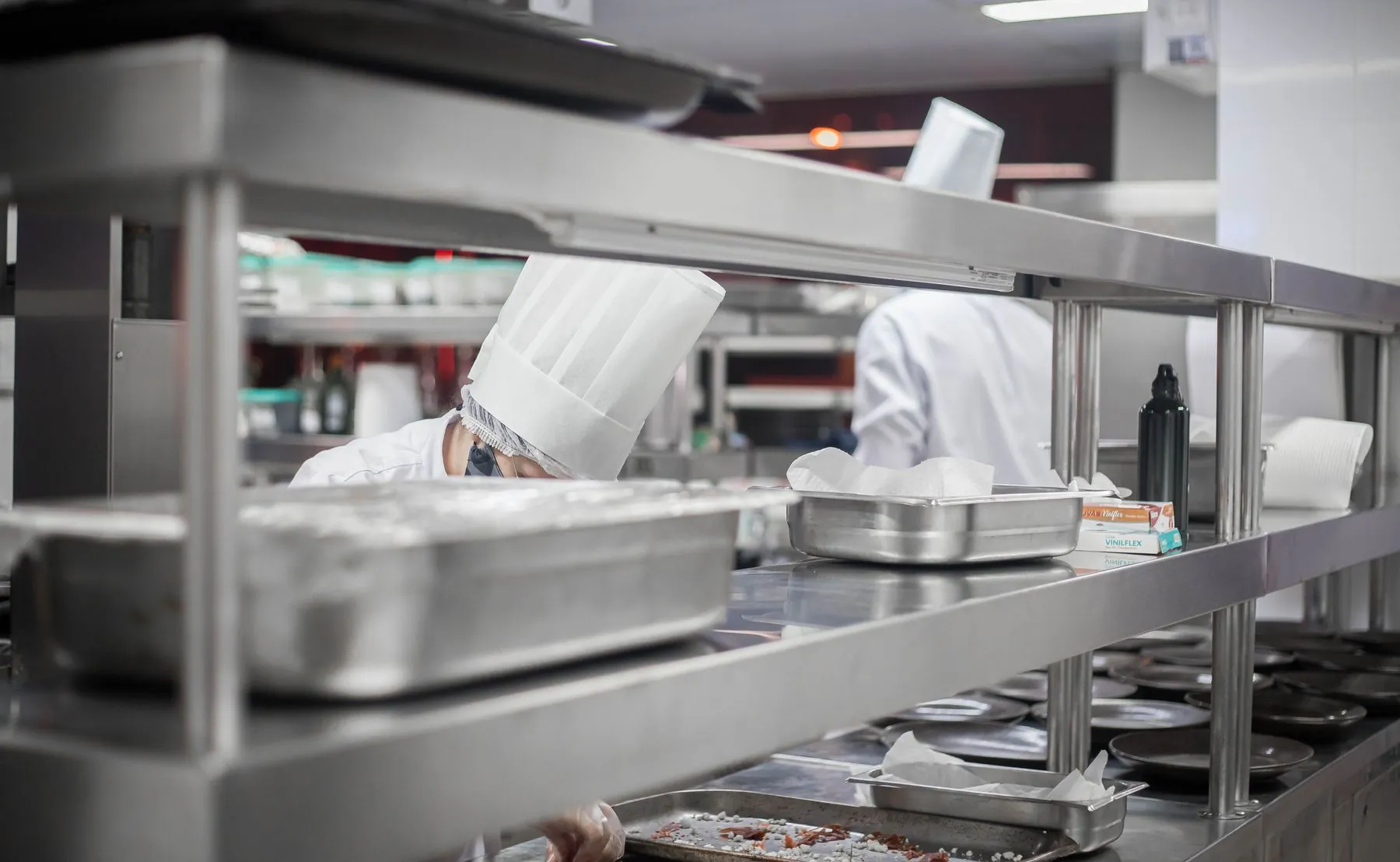 Cooks preparing food in a stainless steel commercial kitchen with overhead shelving